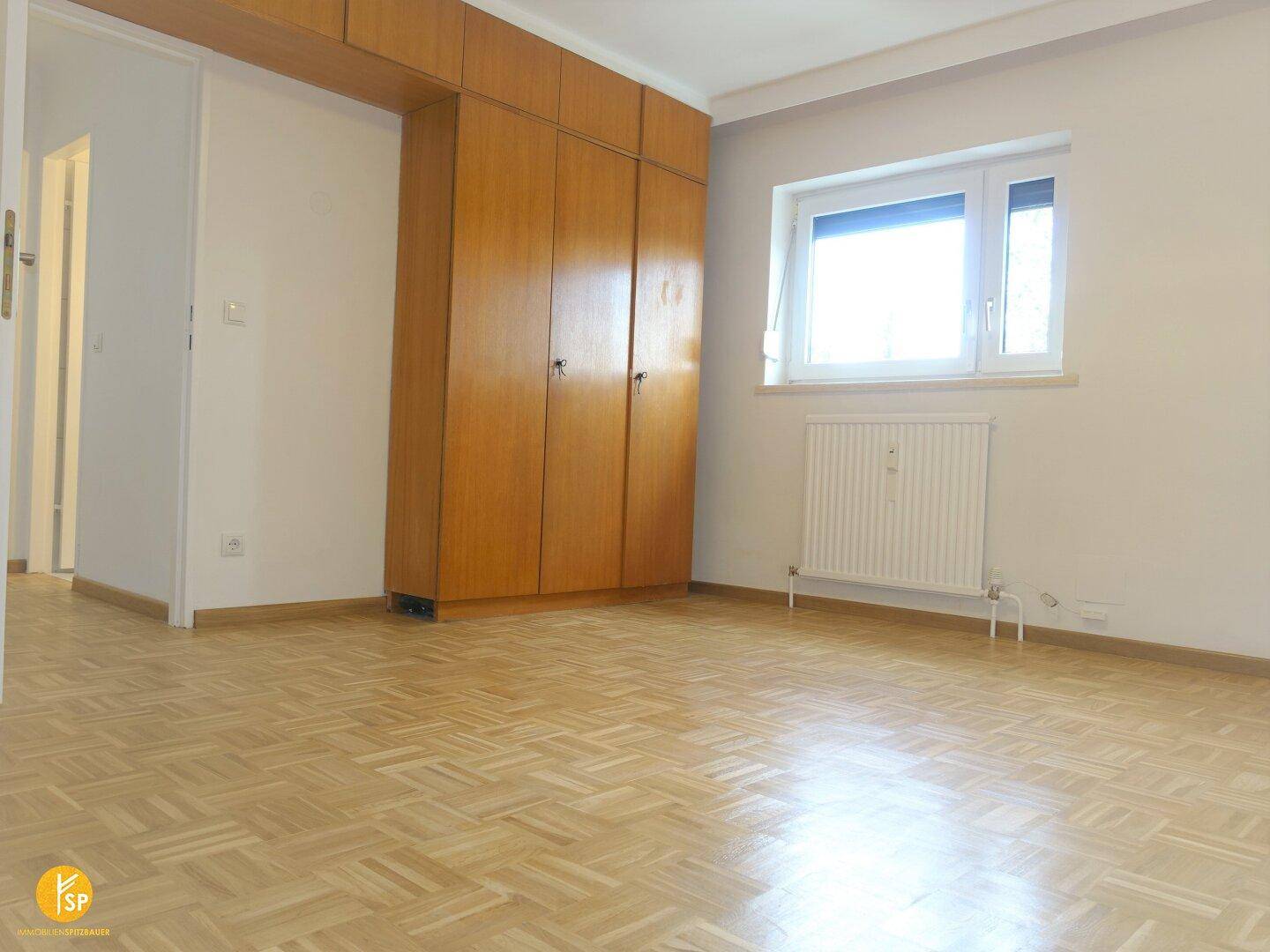 Geräumiges Schlafzimmer mit Einbauschränken, Fenster und glänzendem Holzparkettboden.