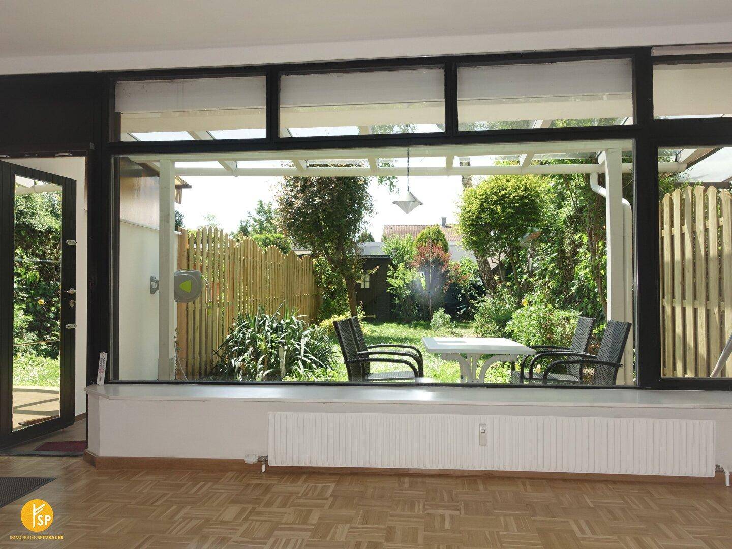 Geräumiges Wohnzimmer mit weitem Blick in den grünen Garten durch große Fenster.