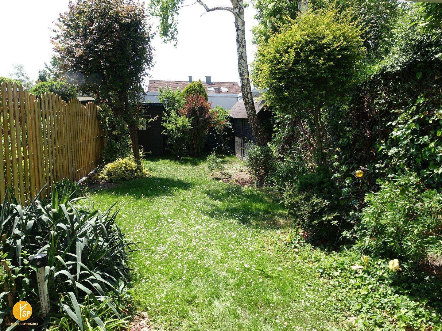 Gepflegter Garten mit Rasenfläche, umzäunt von einem Holzzaun und umgeben von Bäumen.