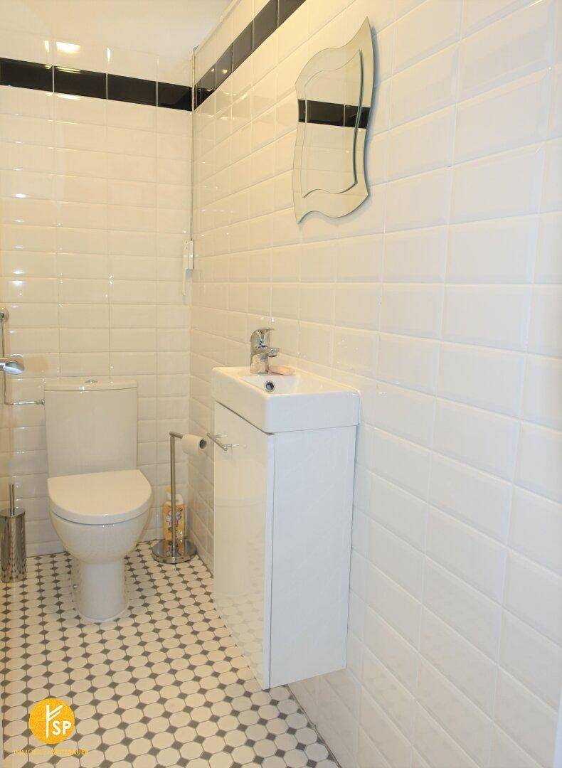 Modern gefliestes Gäste-WC mit wandhängendem Waschbecken und Toilette in hellen Farben.