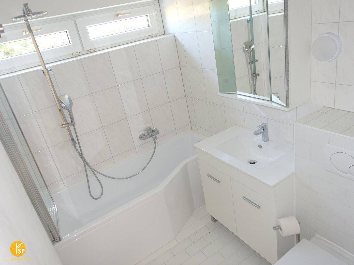 Funktionales Badezimmer mit Badewanne, integrierter Dusche und weißem Fliesenboden.