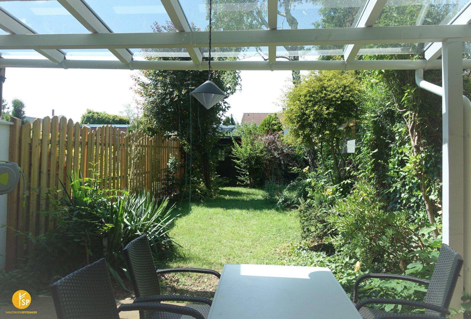 Überdachte Terrasse mit Sitzgelegenheiten und Blick auf den grünen, gepflegten Gartenbereich.