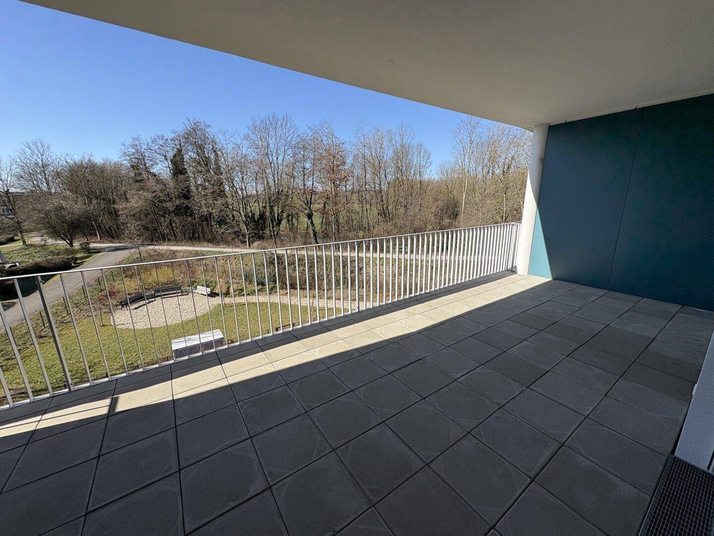 Geräumige geflieste Terrasse mit Blick auf die umliegende Natur und Grünflächen an einem sonnigen Tag.