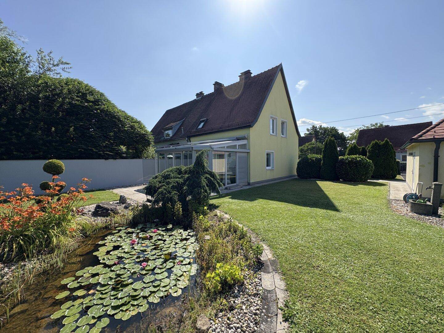 Großer, sonniger Garten mit Teich, Seerosen und Wintergarten am hinteren Teil des Hauses.