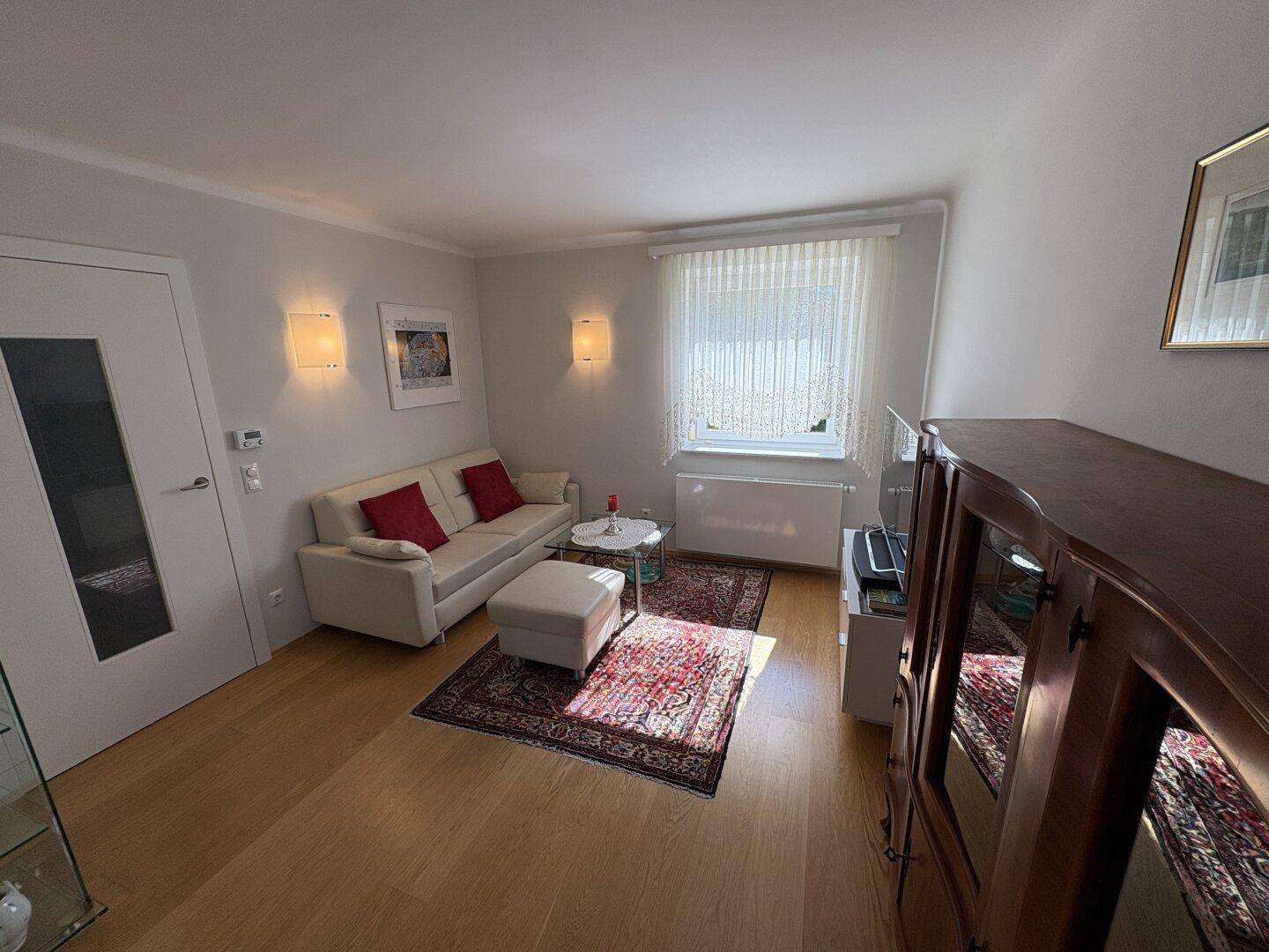 Wohnzimmer mit hellem Sofa, Teppich und einem Schrank, der den Raum gemütlich macht.