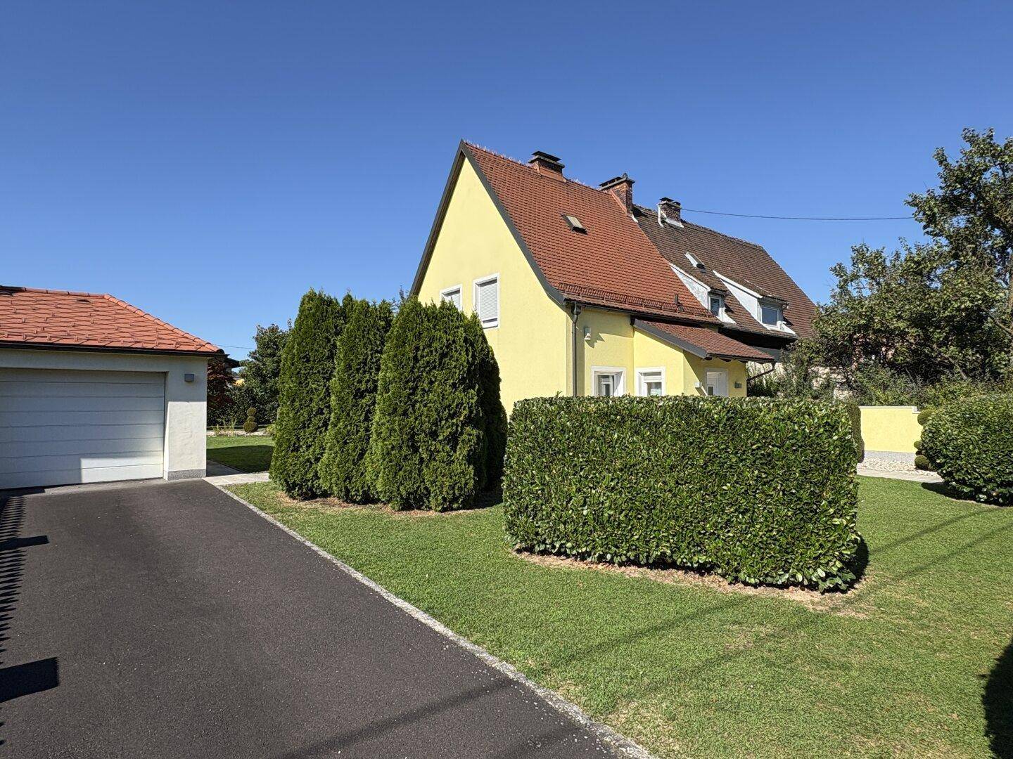 Seitenansicht des Hauses mit Einfahrt, Garage und gepflegter Hecke.
