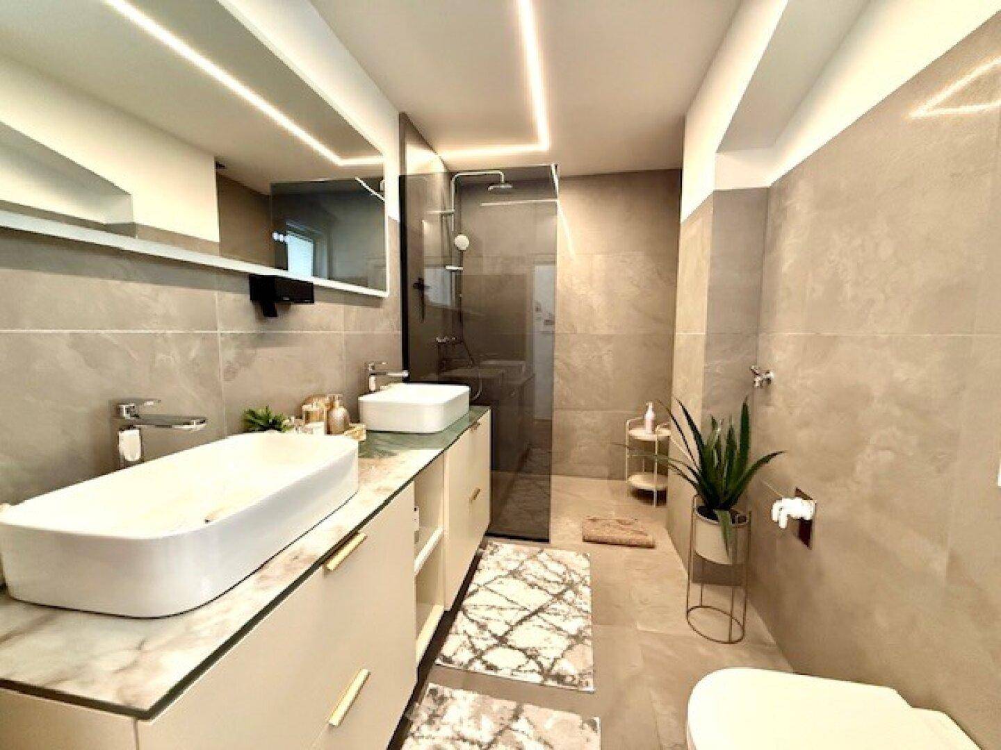 Modernes Badezimmer mit Doppelwaschbecken, begehbarer Dusche und eleganten Fliesen.