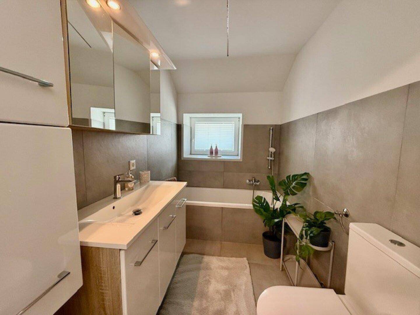 Badezimmer mit Badewanne, Einzelwaschbecken, Spiegelschrank und Fenster für Belüftung.