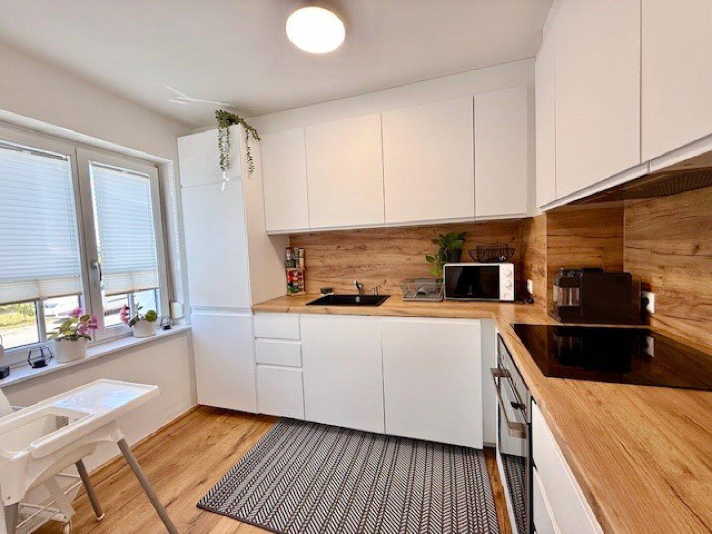 Moderne Küche mit weißen Schränken, Holz-Arbeitsplatten und Fenster für natürliches Licht.