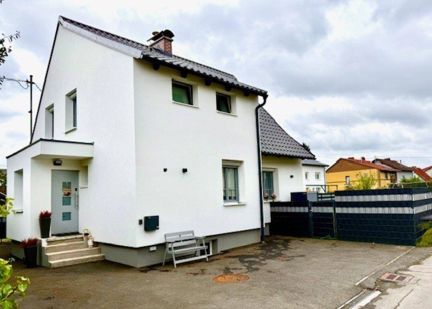 Seitenansicht des Hauses mit Eingangsbereich und gepflasterter Zufahrt unter bewölktem Himmel.
