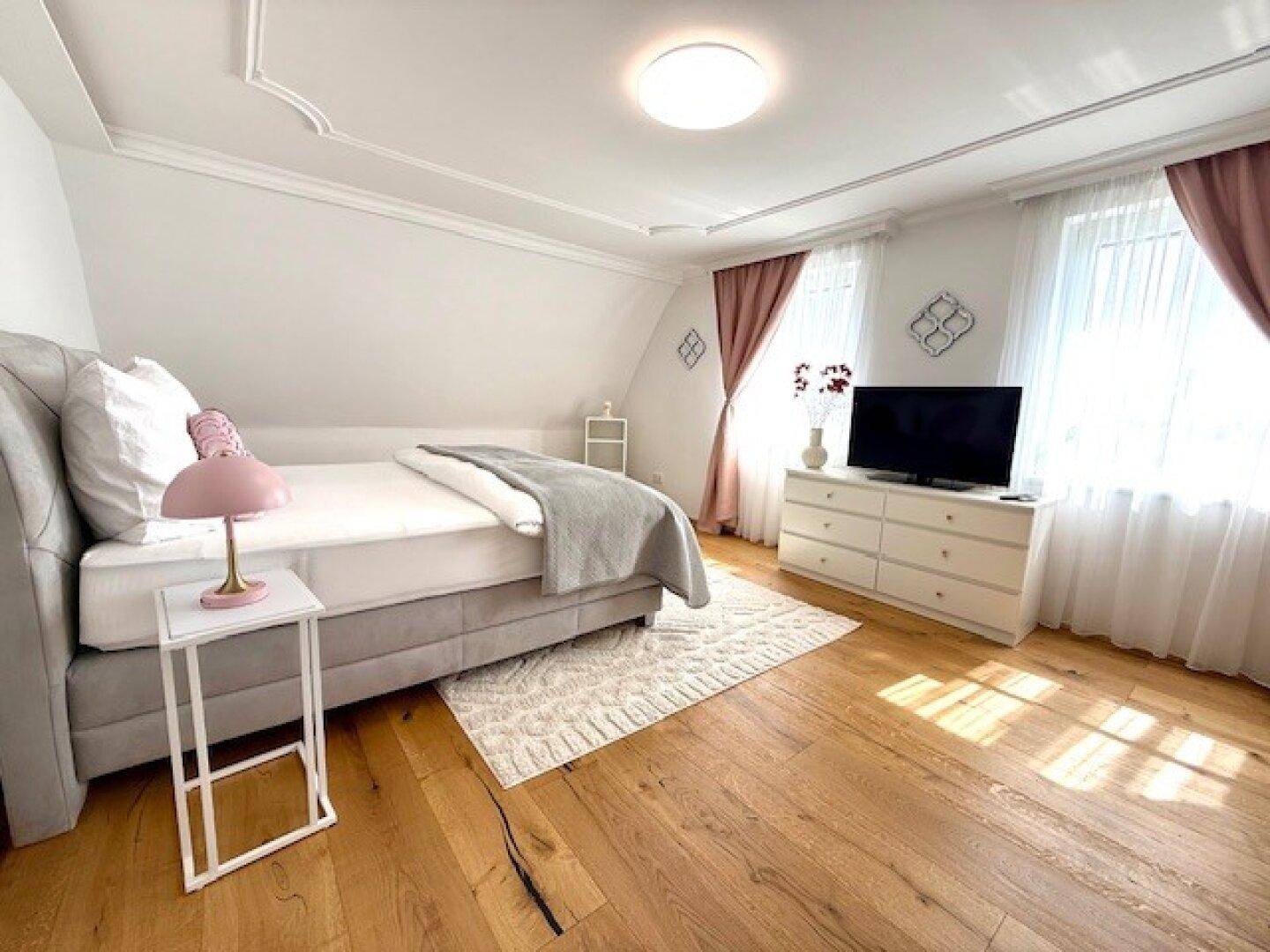 Helles Schlafzimmer mit Dachschräge, Holzboden und modernem Bett mit Nachttischlampe.