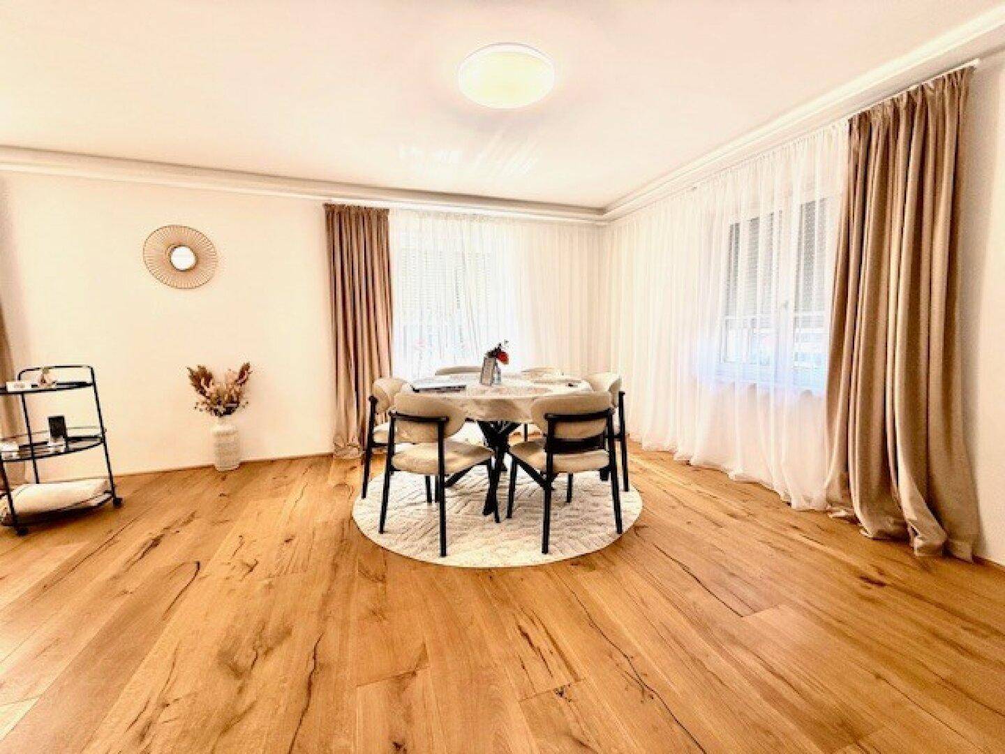 Eleganter Essbereich mit großem Esstisch, Holzboden und Vorhängen in warmen Farbtönen.