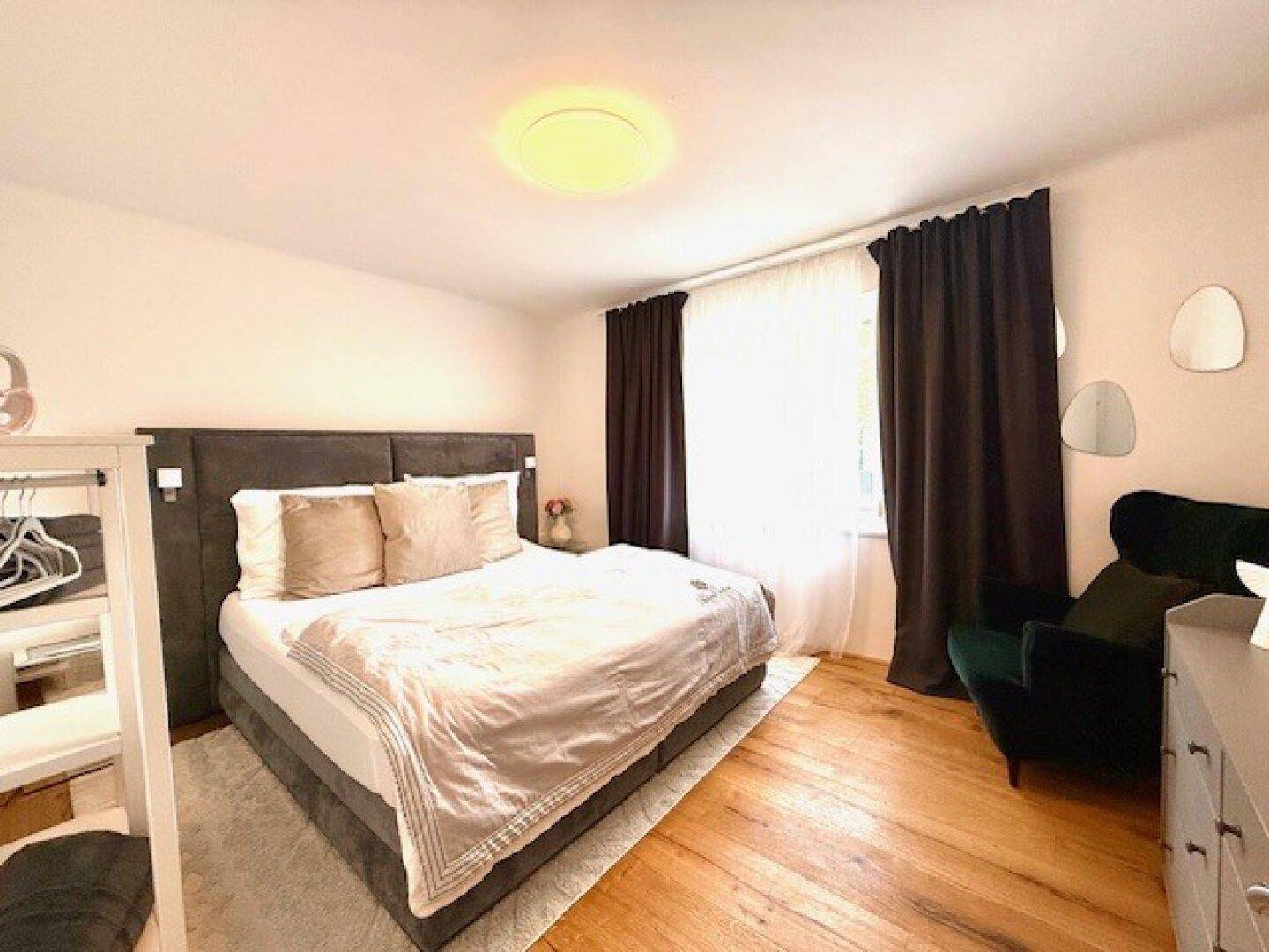 Gemütliches Schlafzimmer mit großem Bett, Holzboden und dunklen Vorhängen für erholsamen Schlaf.