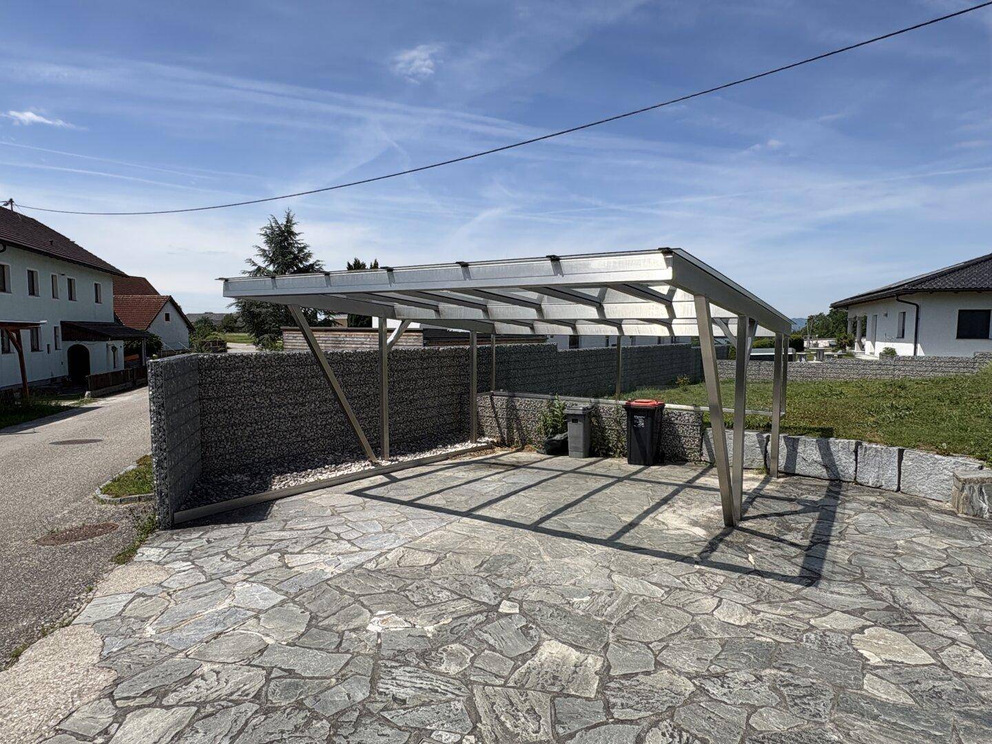 Moderner Carport mit gepflastertem Stellplatz und Gabionenwand im Außenbereich.