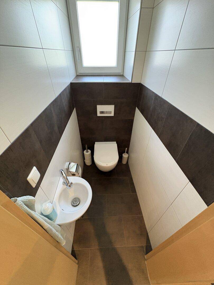 Kleines Gäste-WC mit wandhängendem WC, Handwaschbecken und einem Fenster für Tageslicht.