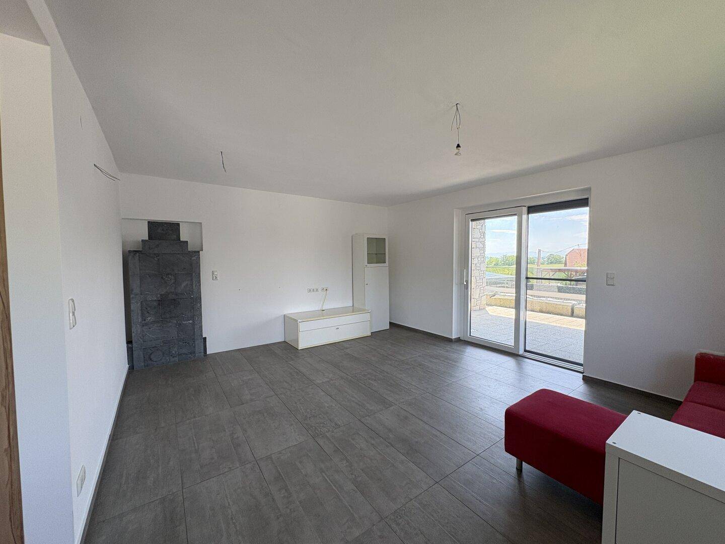 Heller Wohnbereich mit großem Schiebefenster, Kaminofen und Zugang zur Außenterrasse.