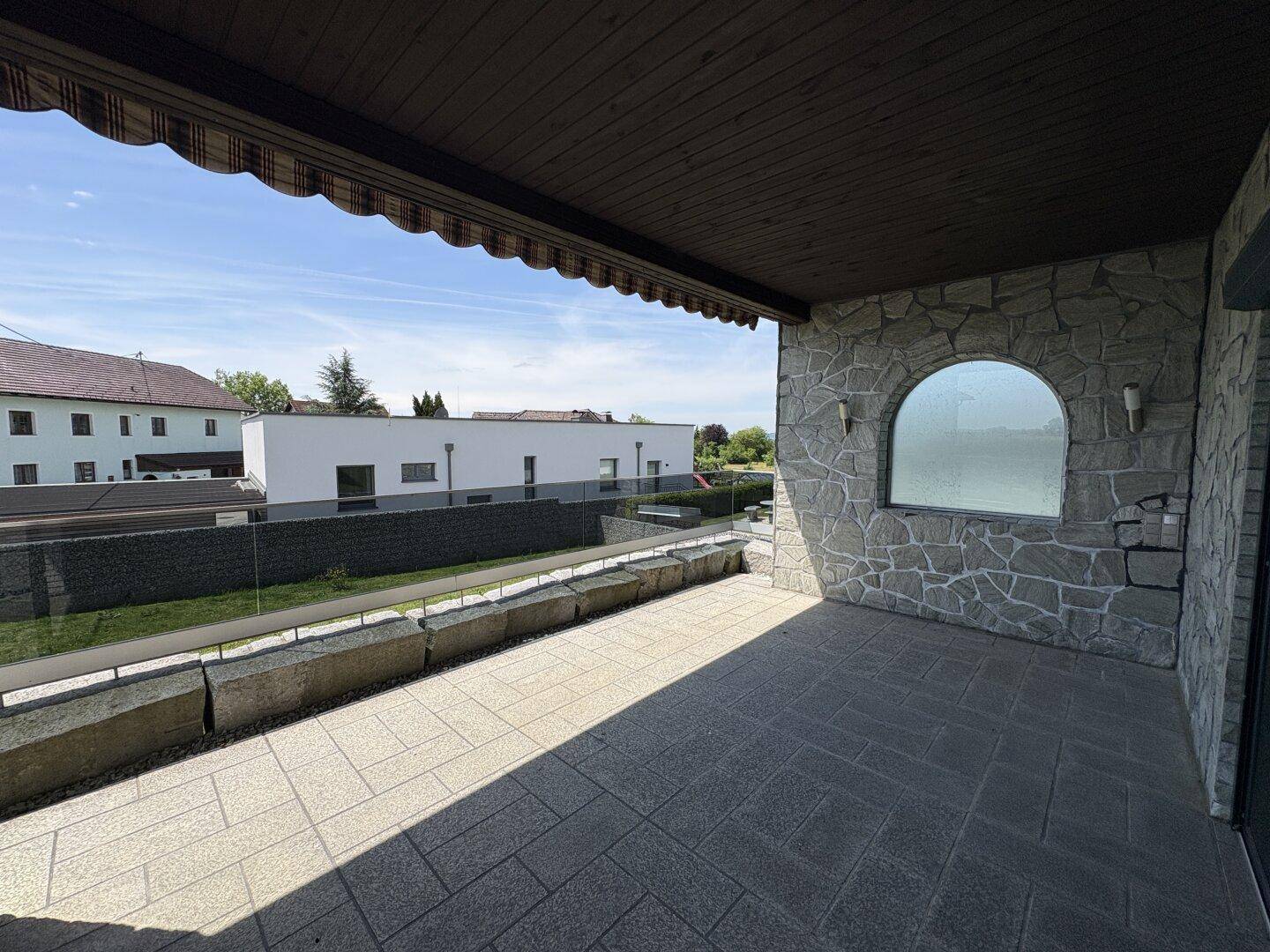 Geräumige Terrasse mit Steinmauer, Fliesenboden und weitem Blick über die Landschaft.