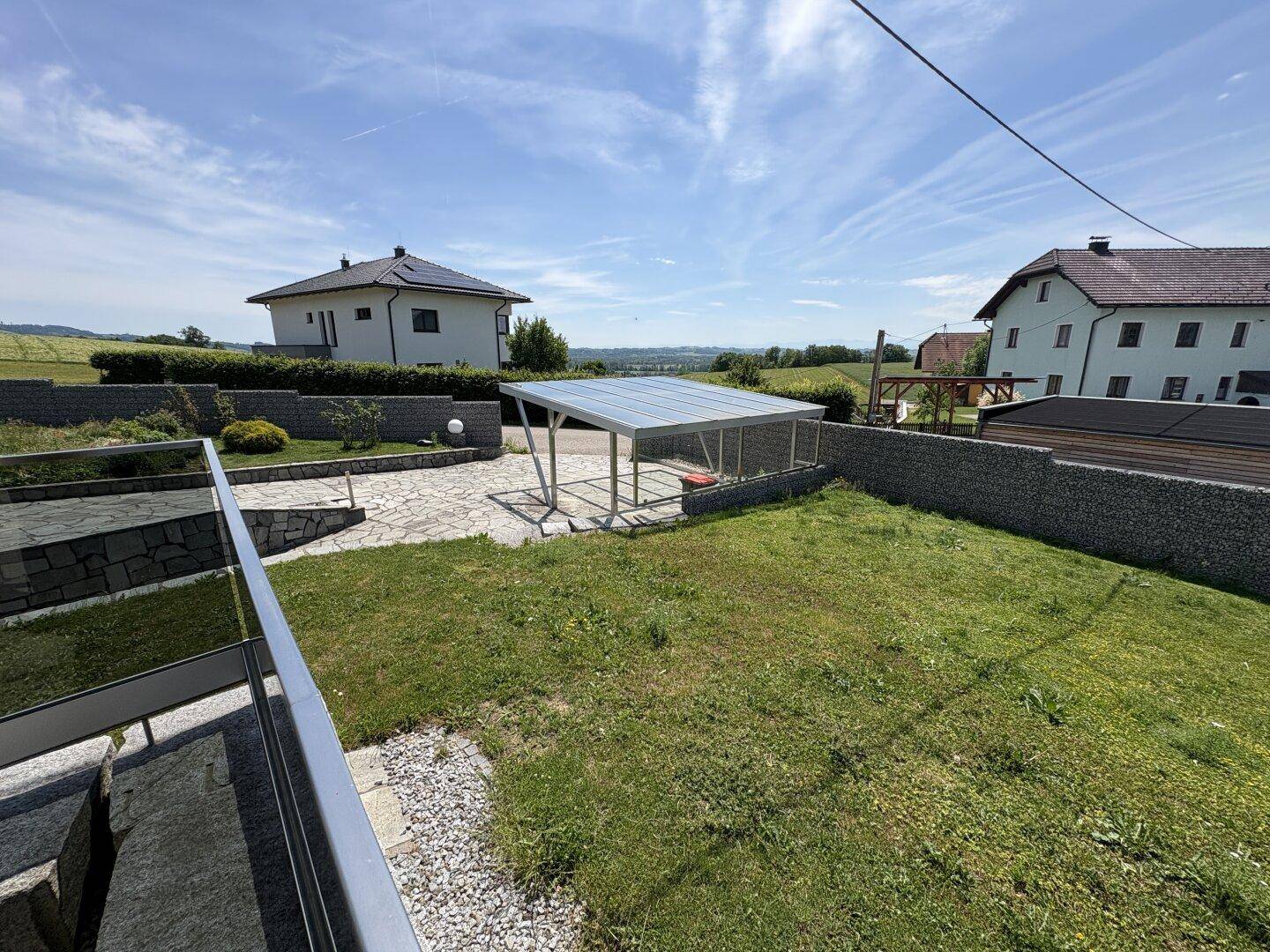 Weitläufiger Gartenbereich mit Rasenfläche, Carport und Panoramablick auf die Landschaft.