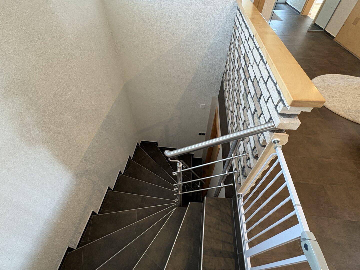 Treppenhaus mit dunklen Fliesen, modernem Metallgeländer und Kinderschutzgitter.