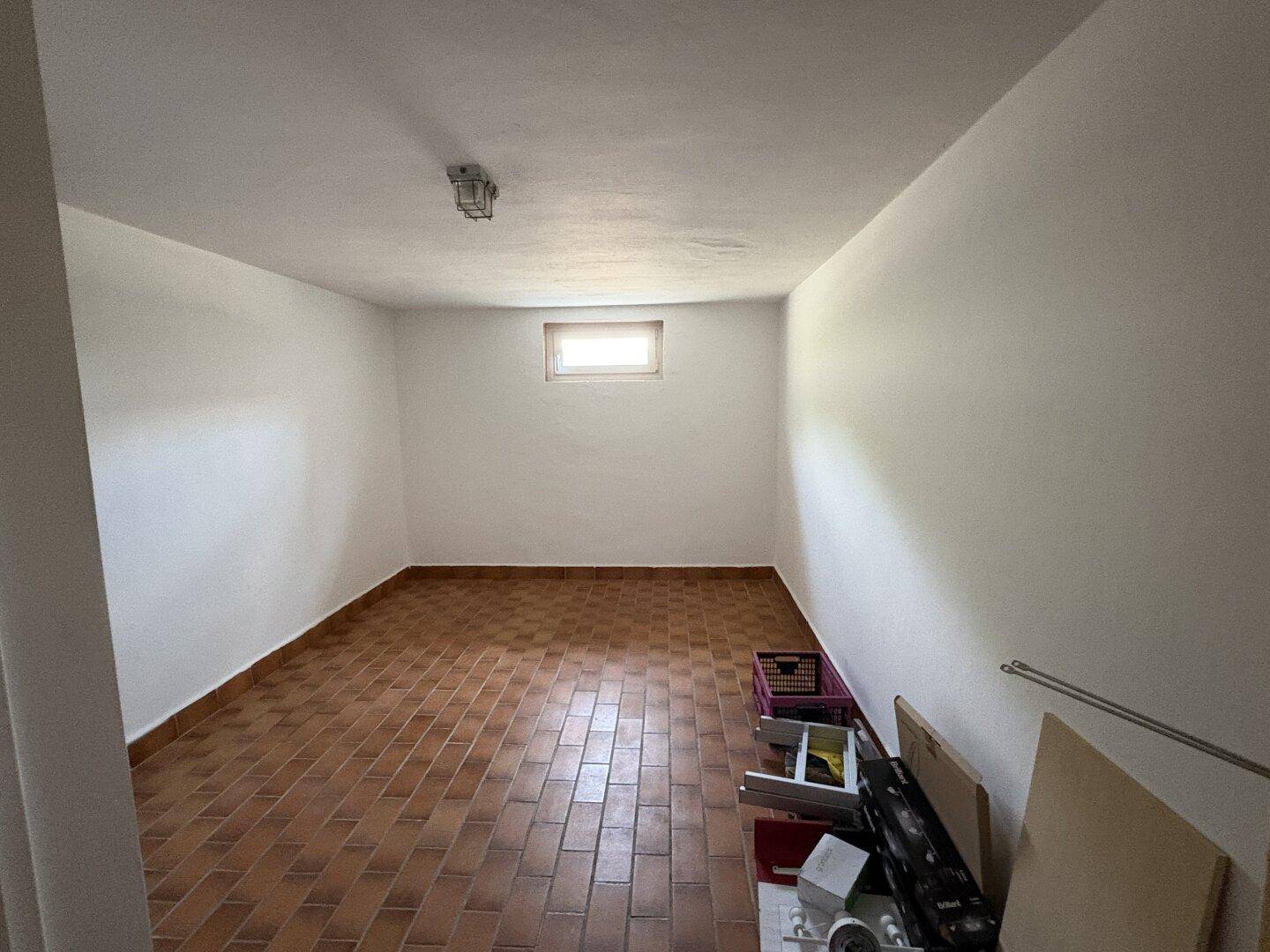 Geräumiger Kellerraum mit Terrakotta-Fliesenboden und kleinem Fenster für Belüftung.
