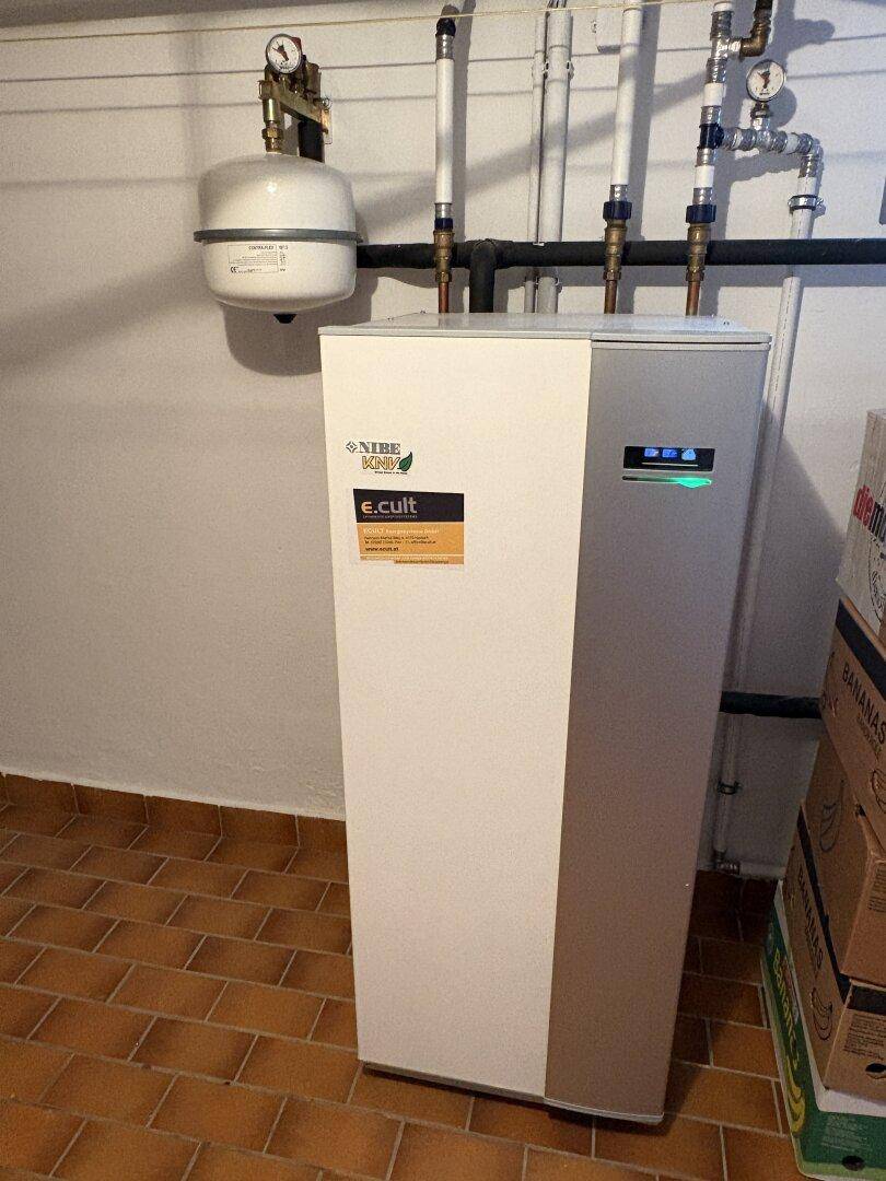 Moderne Wärmepumpe als Heizsystem in einem Technikraum mit Terrakotta-Fliesenboden.