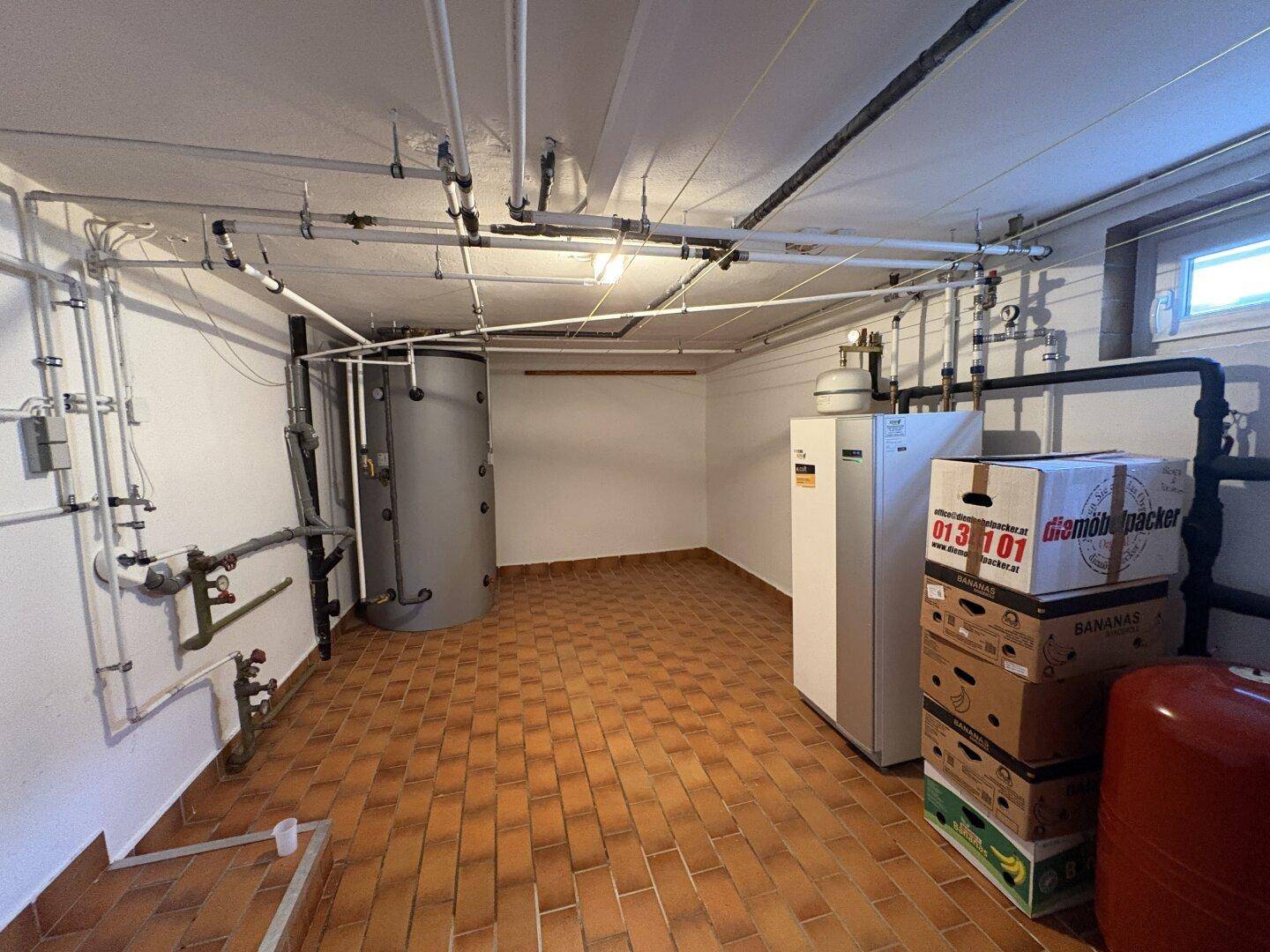 Technikraum im Keller mit Heizungsanlage, Rohrleitungen und Stauraum.