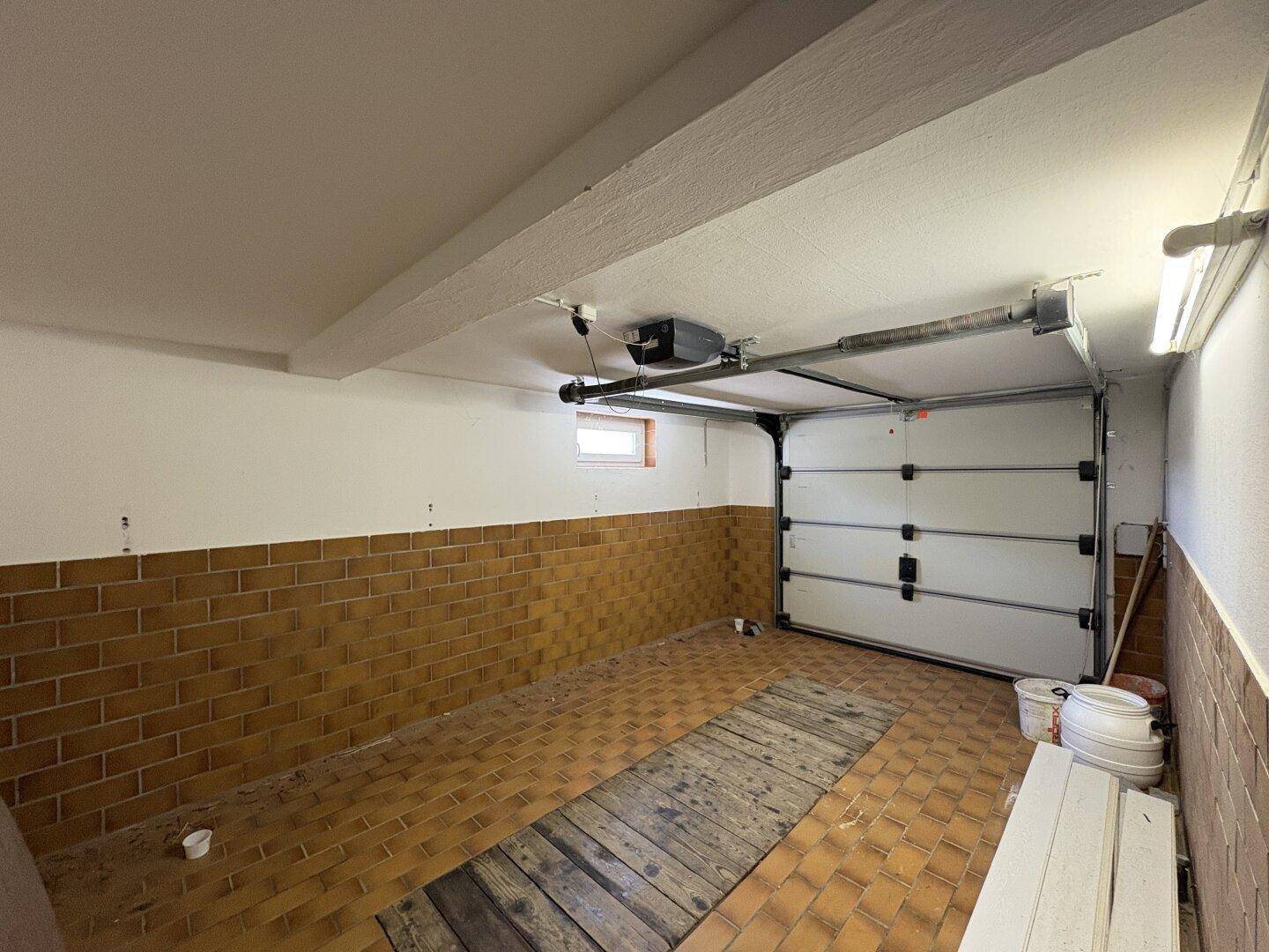 Geräumige Garage mit automatischem Tor, Fliesenboden und kleinem Fenster.