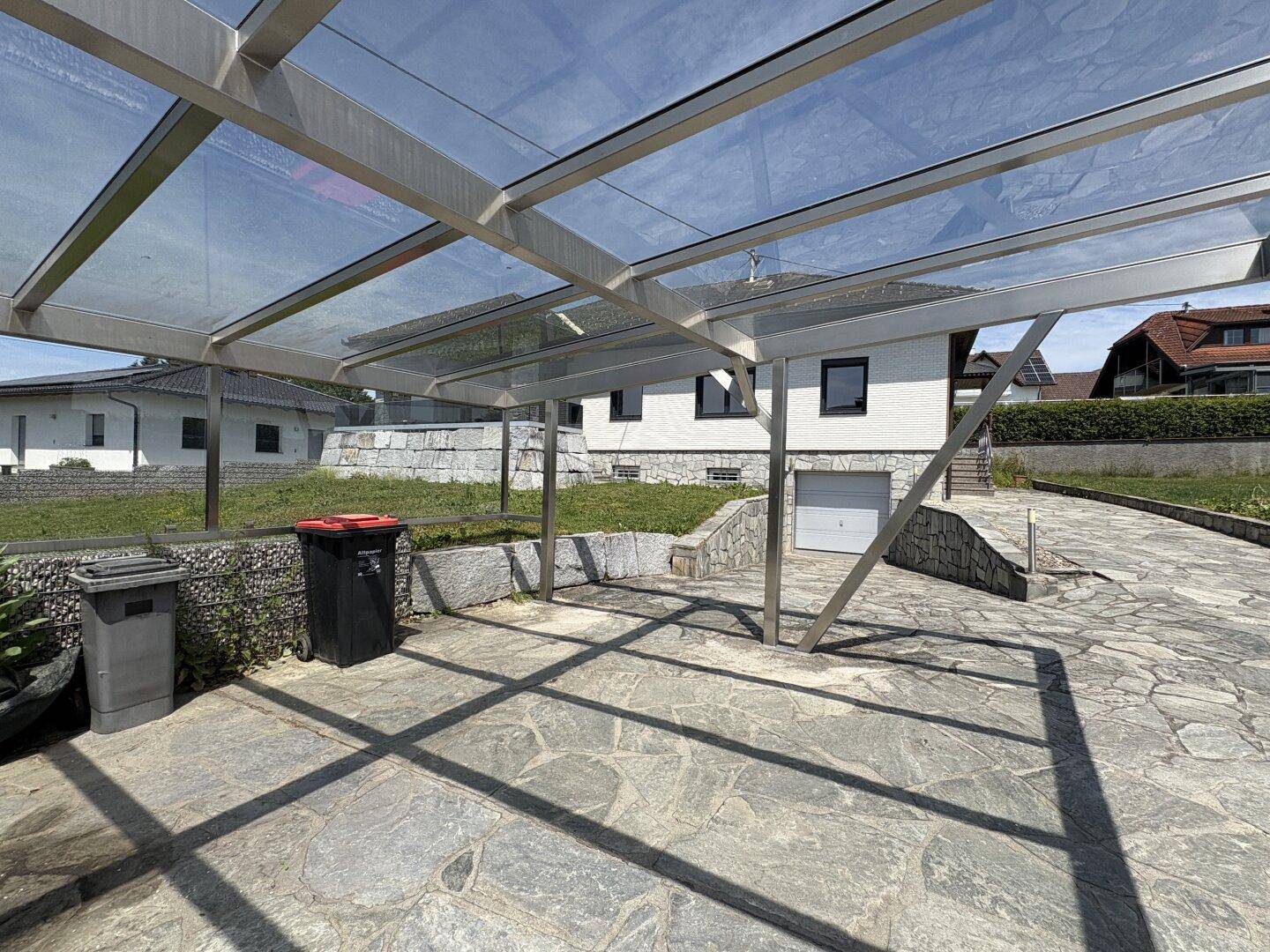 Moderner Carport mit transparentem Dach und gepflastertem Stellplatz vor dem Haus.