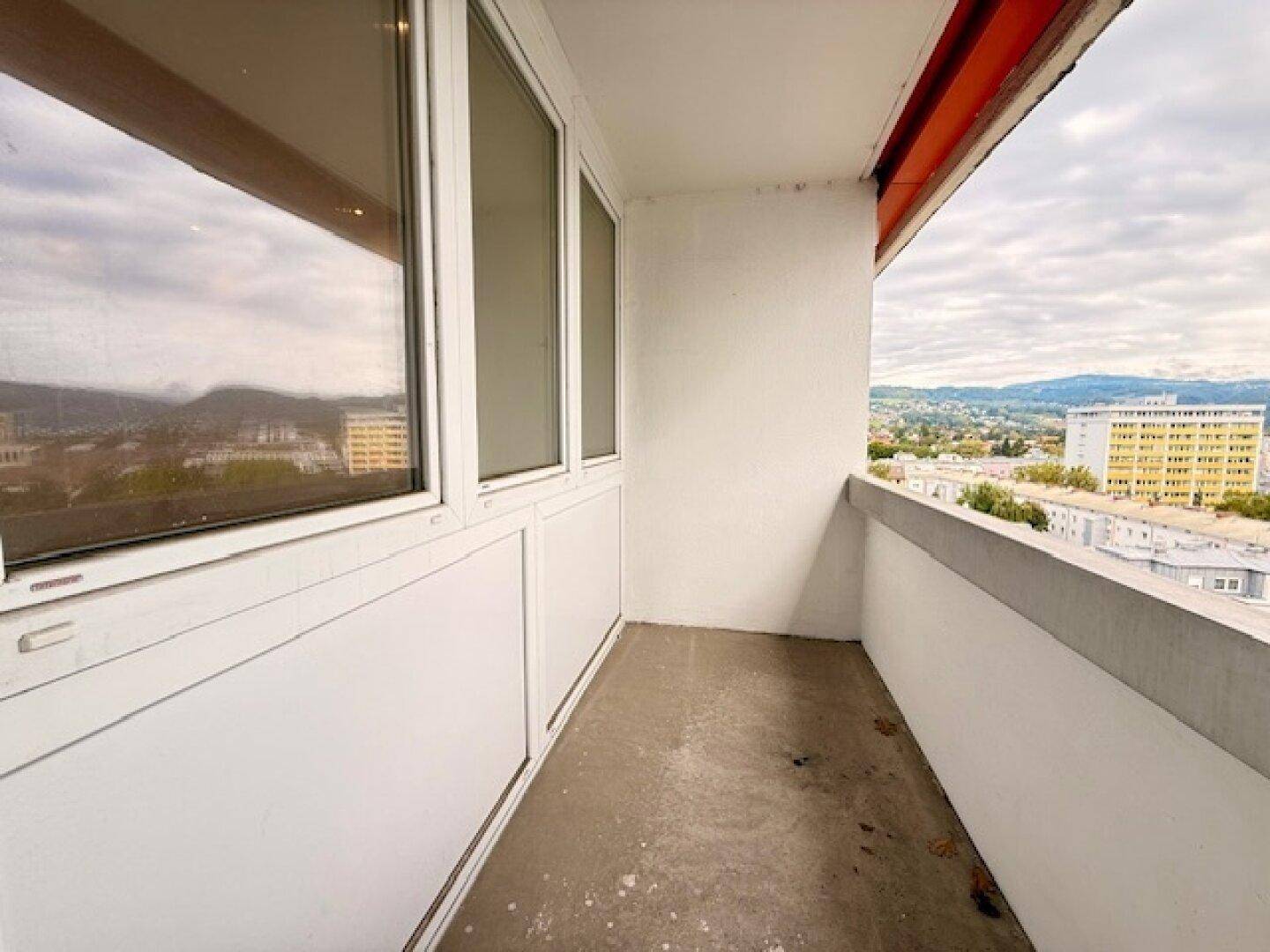 Schmaler Balkon mit Stadtblick und Betonboden, ideal für eine kleine Sitzecke im Freien.