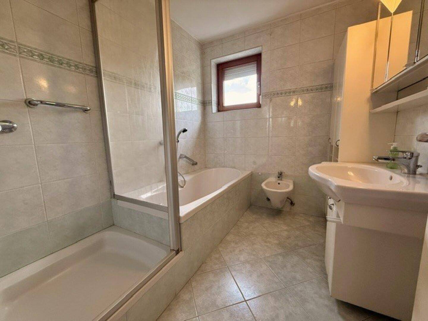 Gefliestes Badezimmer mit Badewanne, Dusche, Bidet und Fenster.
