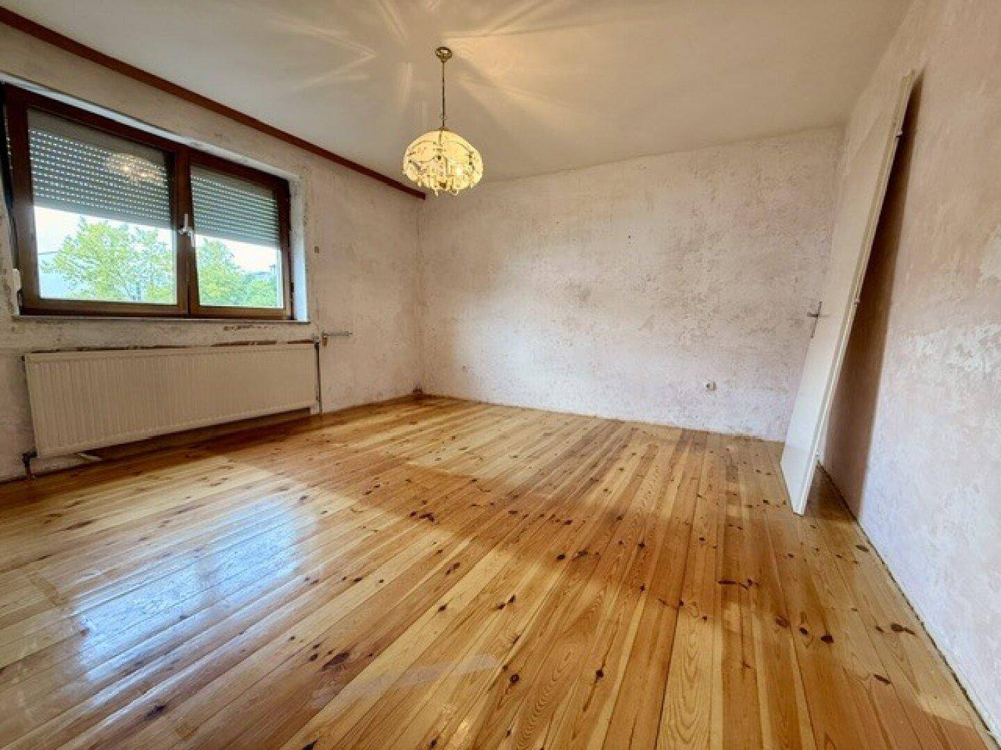 Geräumiges Zimmer mit Holzdielenboden, Fenster und Heizkörper, ideal für eine Neugestaltung.