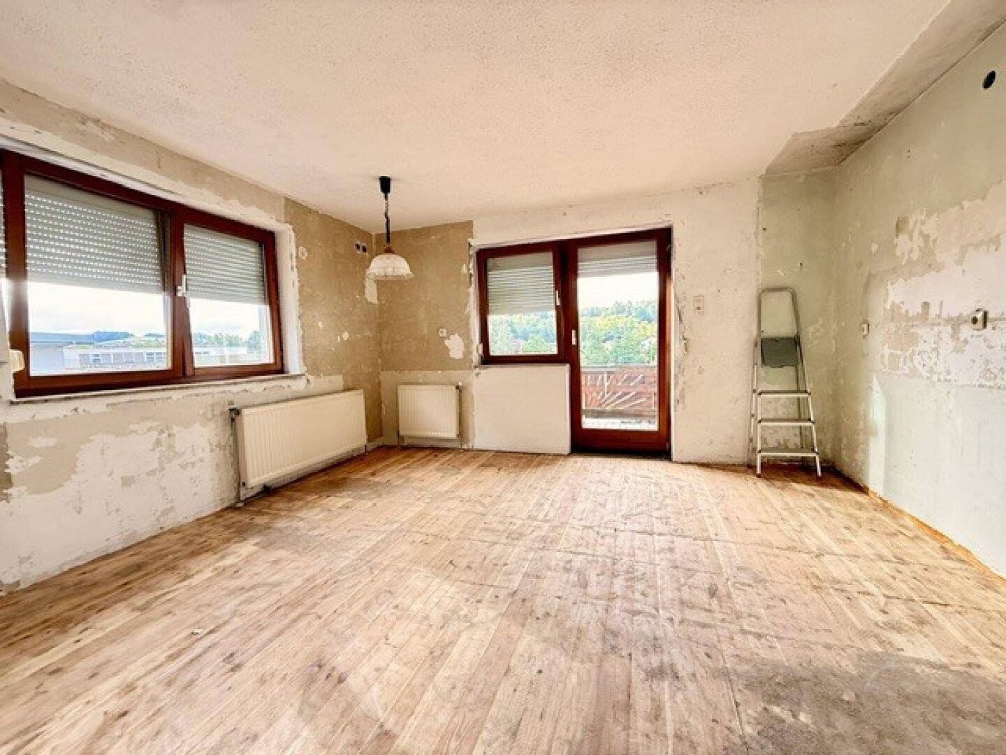 Renovierungsbedürftiges Zimmer mit Holzdielenboden und Zugang zu einem Balkon.