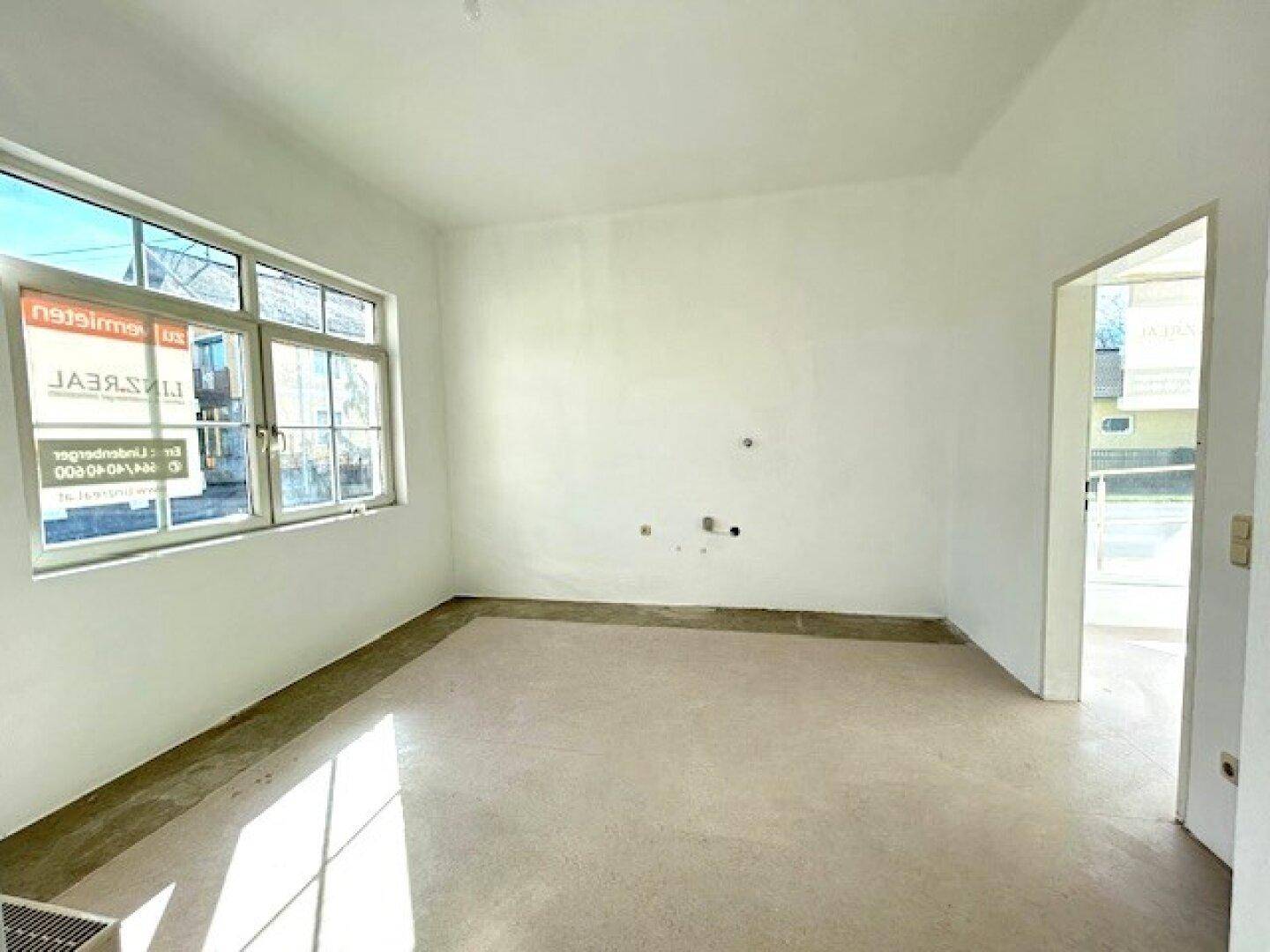 Heller, leerer Raum mit weißen Wänden und Betonboden, ideal für Renovierungsprojekte.