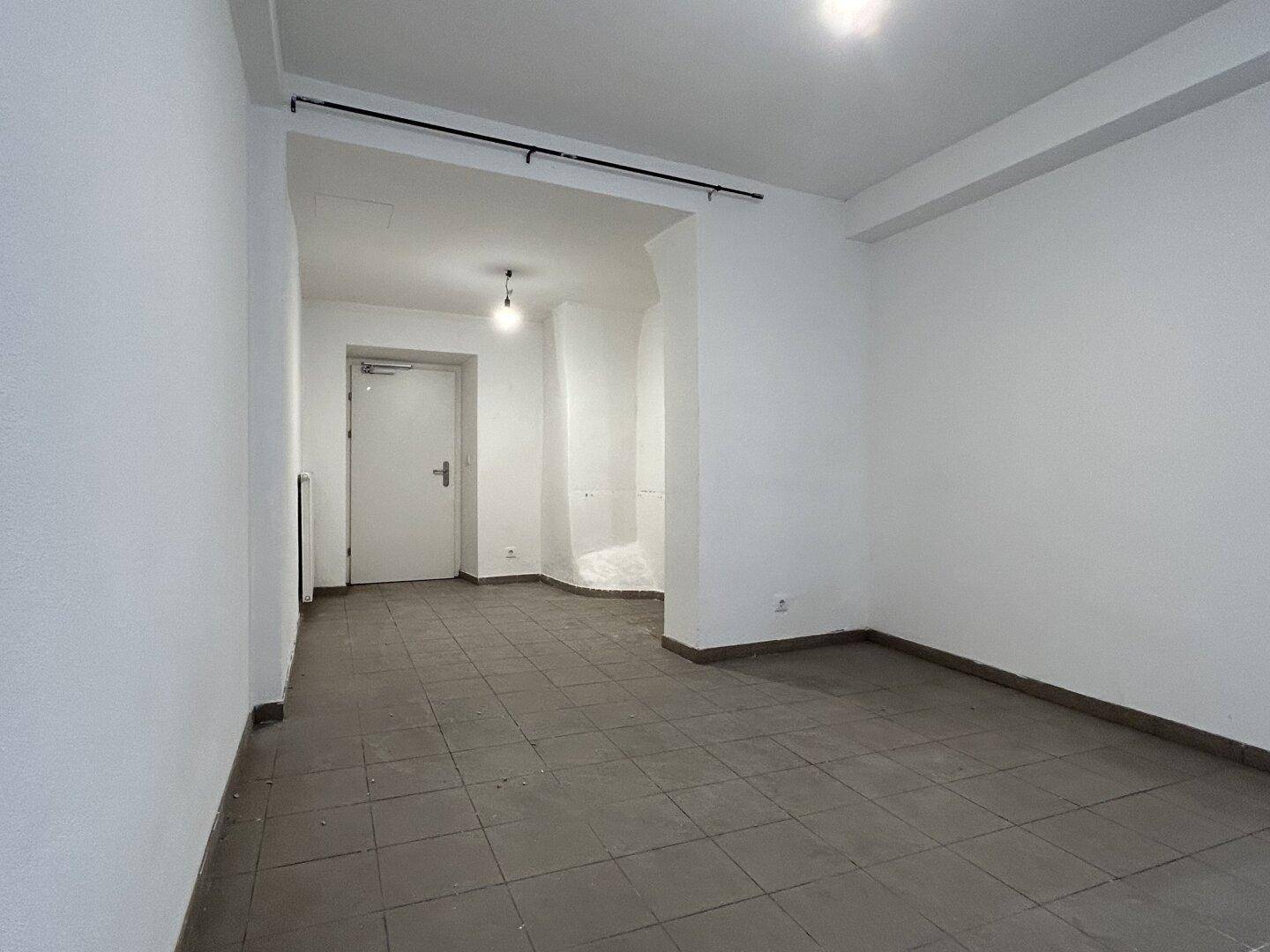 Leerer Gewerberaum mit weißen Wänden, Fliesenboden und einer Tür im Hintergrund.