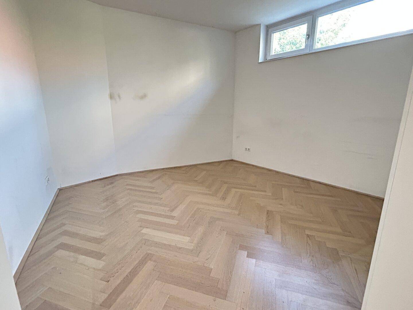 Helles Schlafzimmer mit Fischgrätparkett und einem Fenster für natürliche Belichtung.