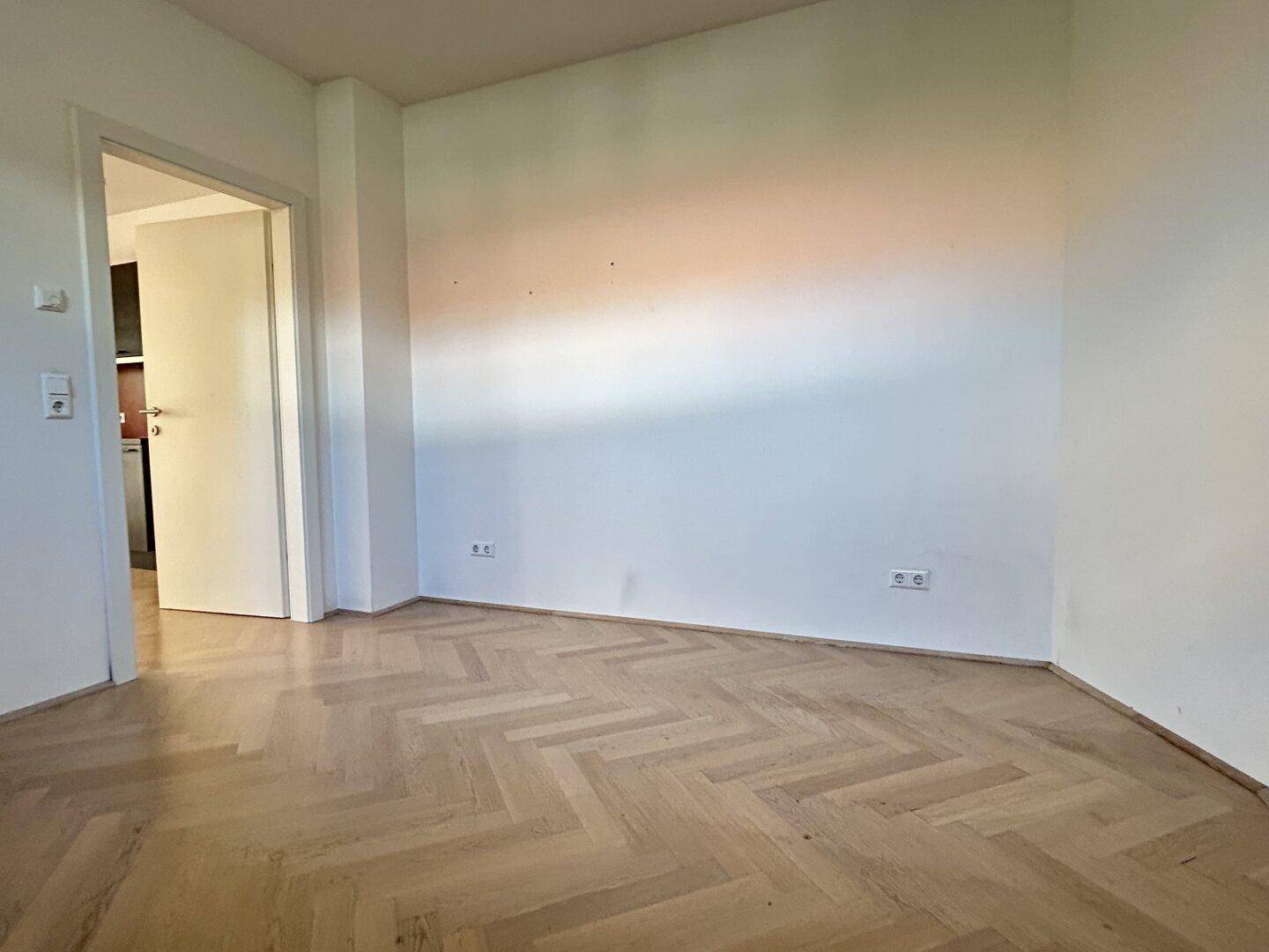 Leeres Zimmer mit Fischgrätparkett und weiß gestrichenen Wänden, bereit zur individuellen Gestaltung.