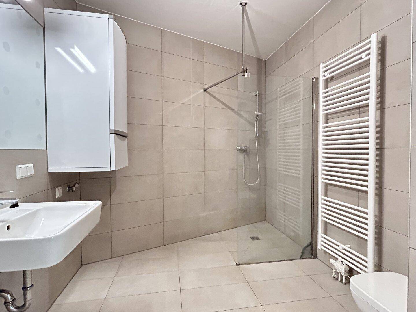 Modernes Badezimmer mit begehbarer Dusche, hellen Fliesen und beheiztem Handtuchhalter.