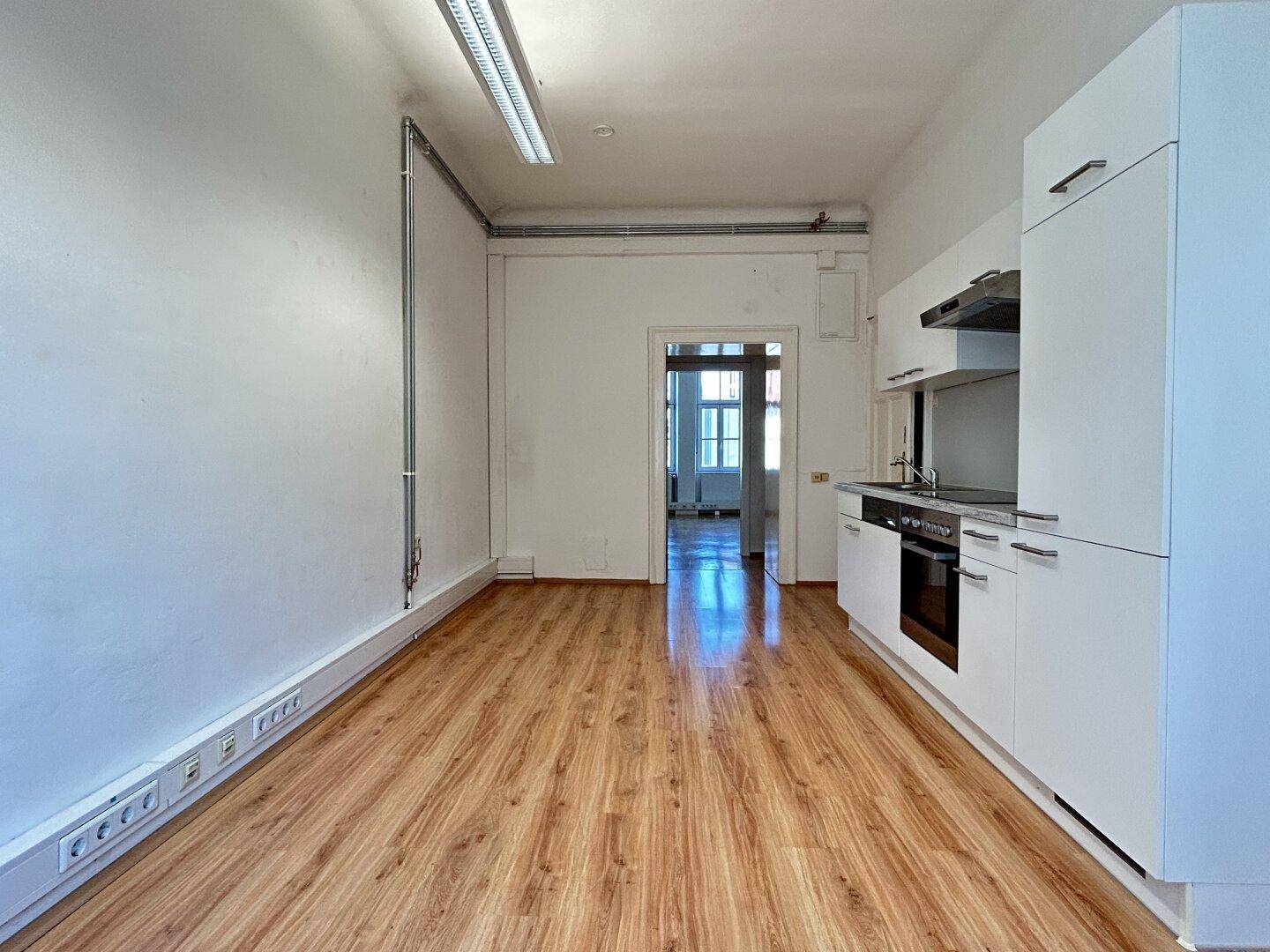Heller Raum mit integrierter Küchenzeile und Zugang zu einem weiteren Zimmer.