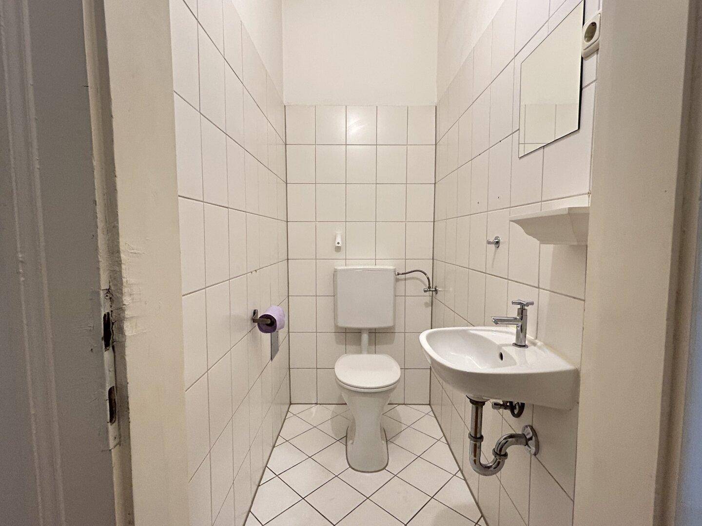 Separates WC mit Toilette, kleinem Waschbecken und weißen Wandfliesen.