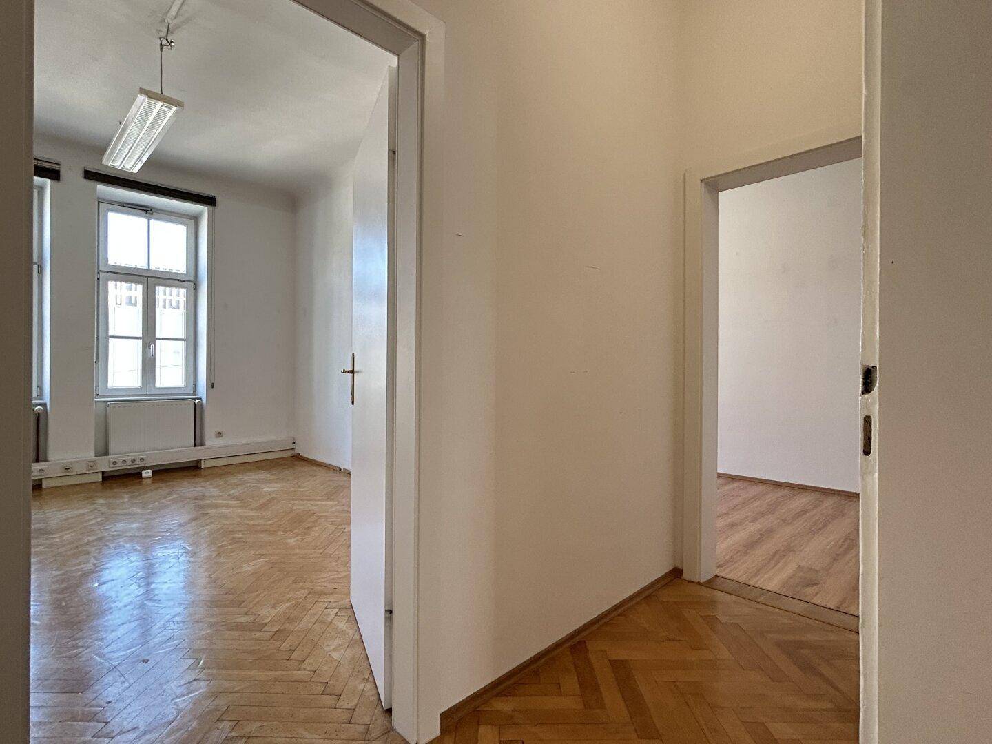 Durchgangsbereich mit Fischgrätparkett, der zwei helle Zimmer miteinander verbindet.