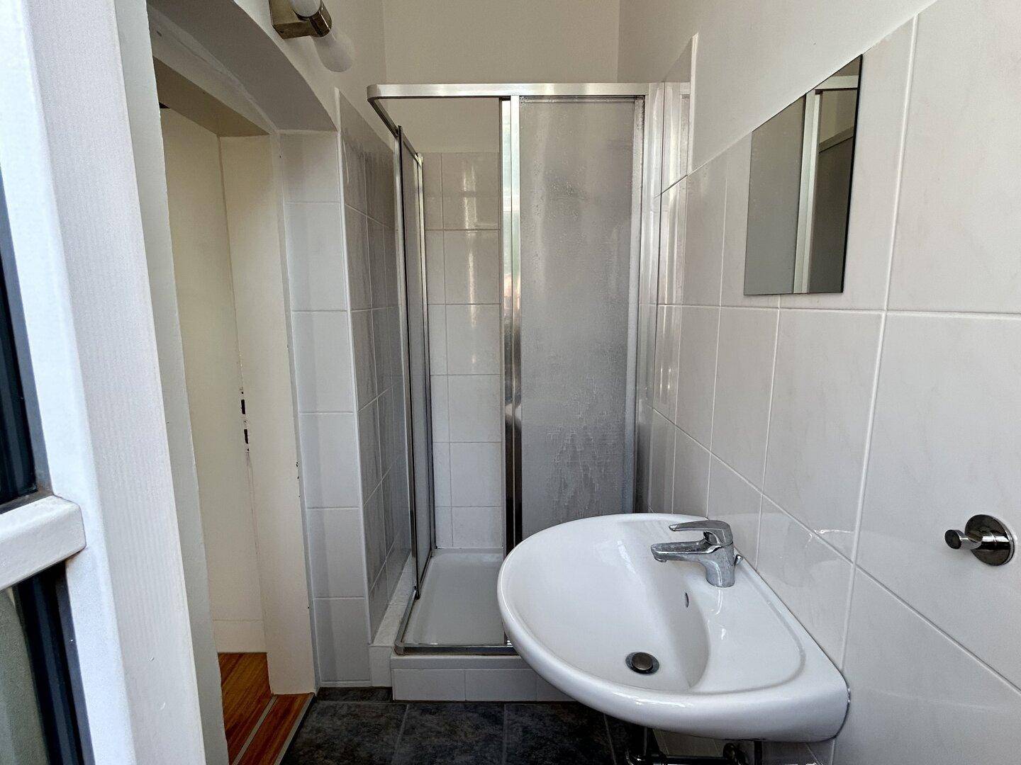 Badezimmer mit Duschkabine, Waschbecken und weißen Fliesen.