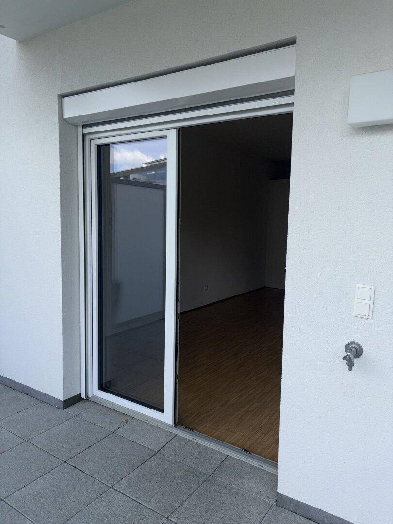 Terrasse mit Schiebetür, die den Blick auf den Innenraum mit Parkettboden freigibt.