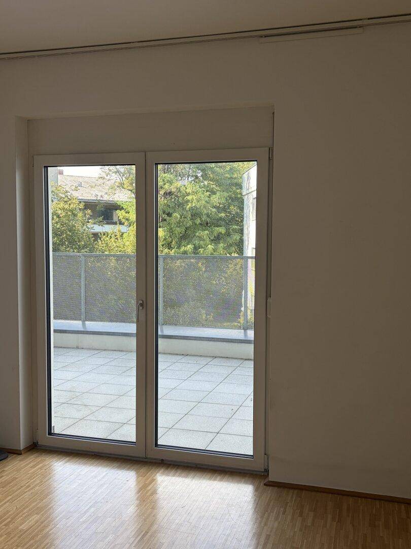Heller Wohnraum mit Parkettboden und Zugang zur Terrasse mit Blick ins Grüne.