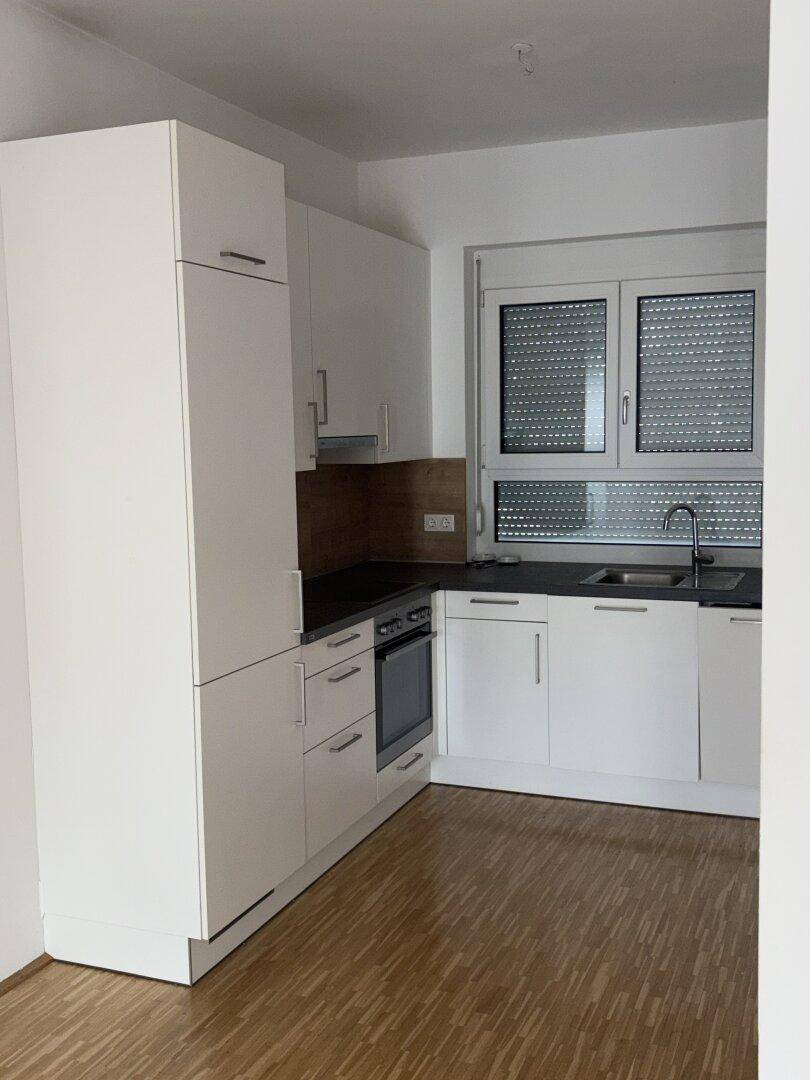 Moderne Küchenzeile mit weißen Schränken, Backofen und dunkler Arbeitsplatte.
