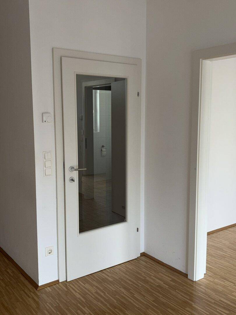 Heller Flur mit Parkettboden und einer Tür mit Glaseinsatz zu einem weiteren Raum.
