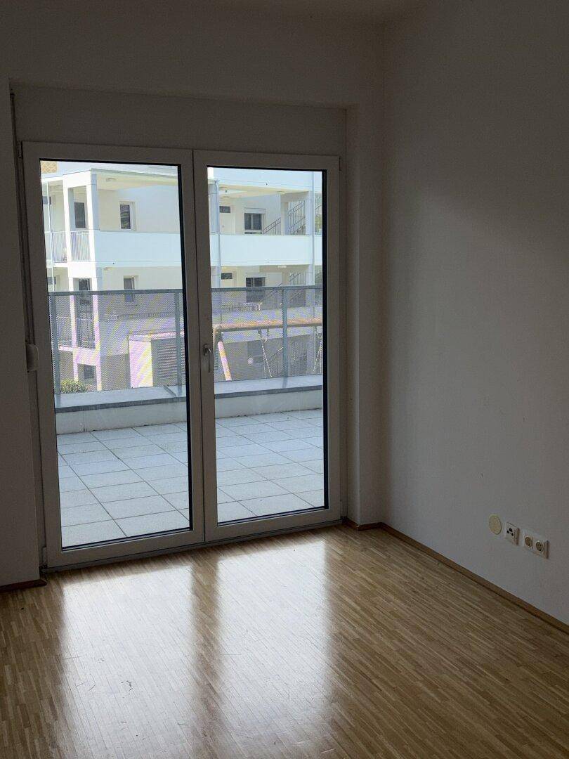 Helles Schlafzimmer mit Parkettboden und großem Fenster mit Blick auf die Umgebung.