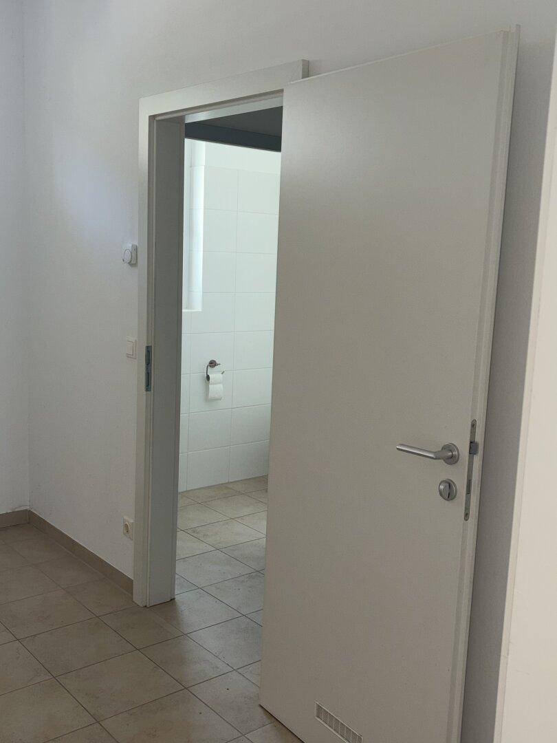 Offene Tür zu einem Badezimmer mit weißen Fliesen und Toilette.