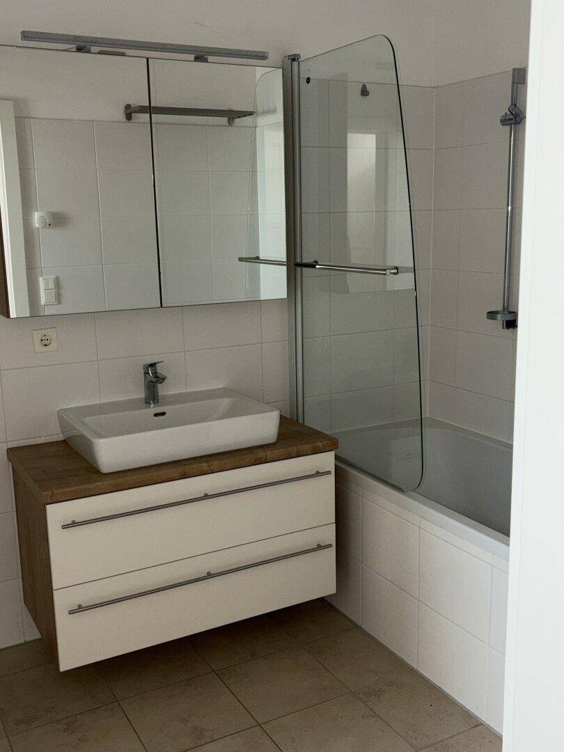 Badezimmer mit Waschtisch, Spiegelschrank und Badewanne mit Duschabtrennung.