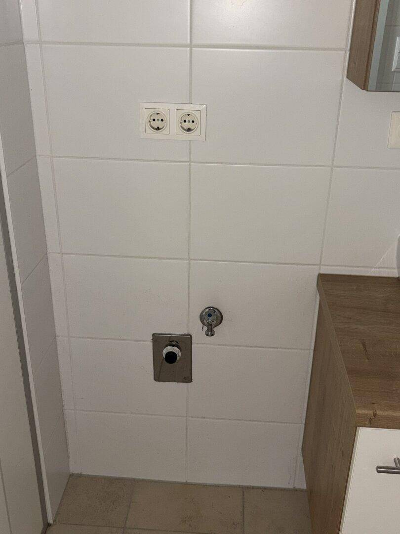 Wandbereich im Badezimmer mit Anschlüssen für eine Waschmaschine.