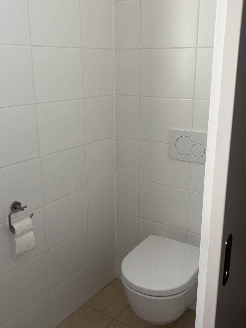 Separate Toilette mit wandhängendem WC und weißen Wandfliesen.